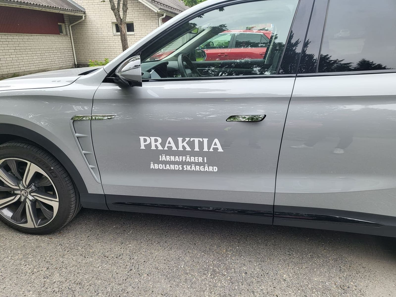 Vit Praktia-logotyp monterad på dörren till en grå bil