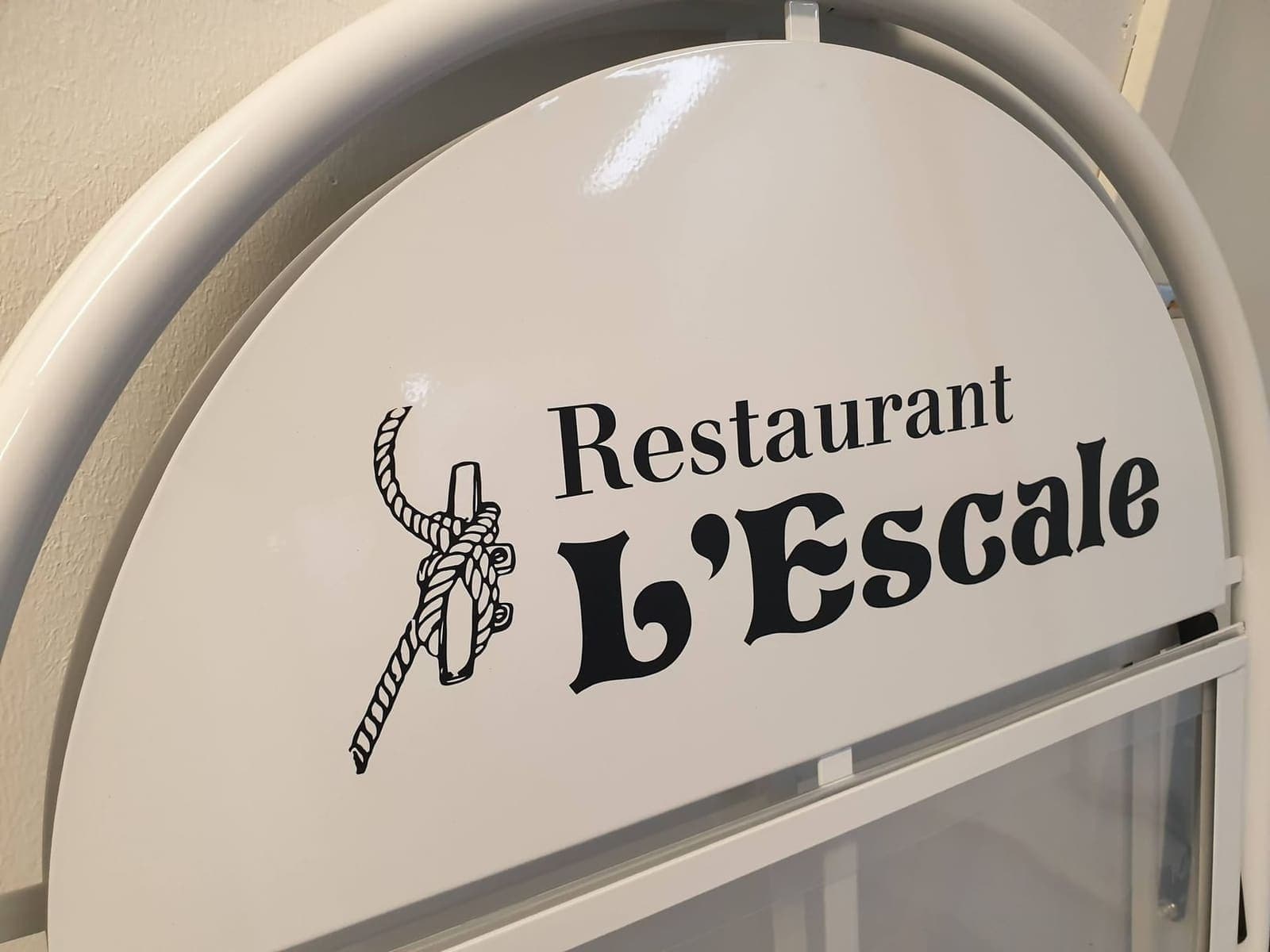 Vit rundad skylt med svart logotyp och texten Restaurant L'Escale